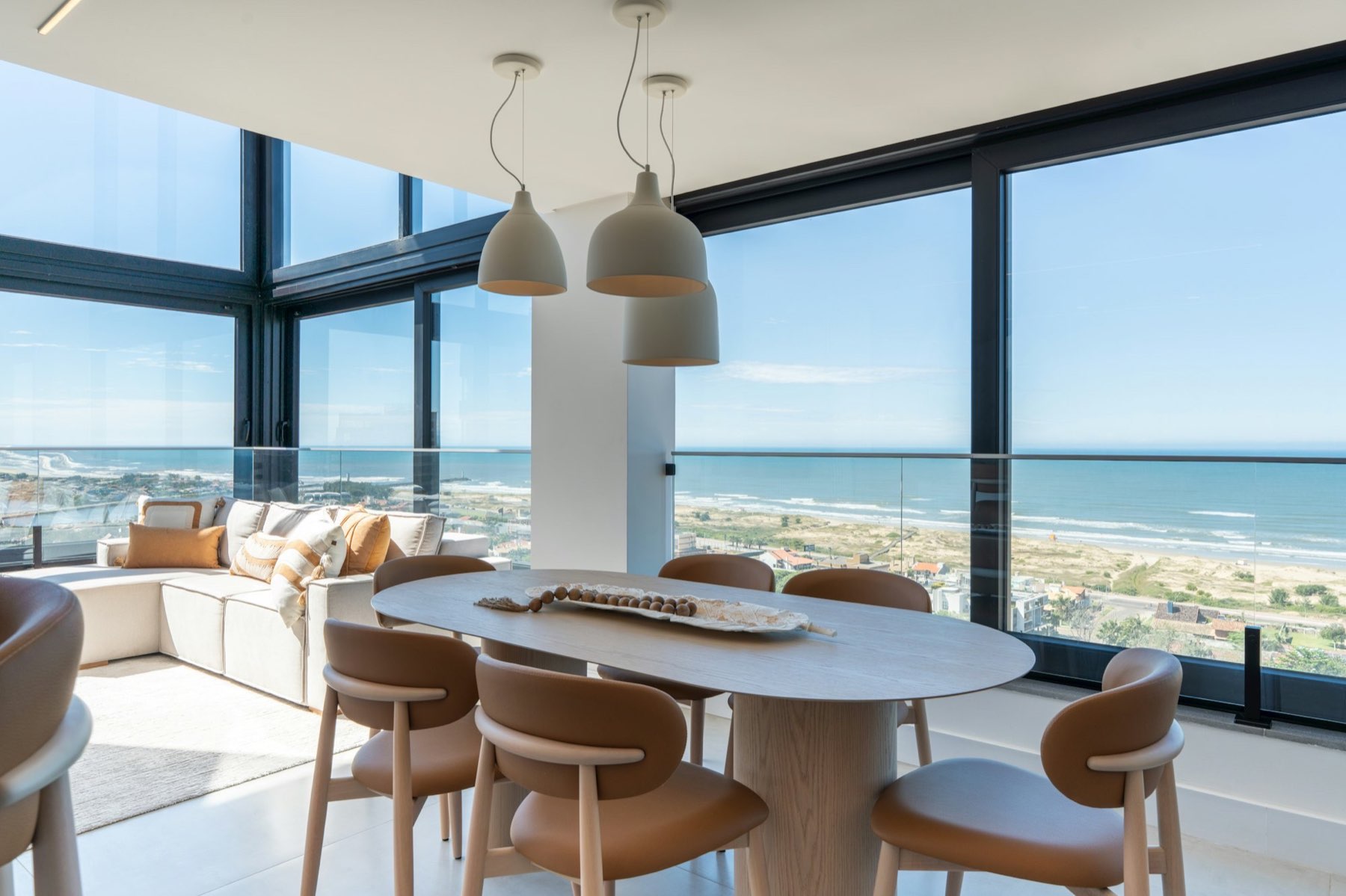 Ocean-view great room with floor-to-ceiling glass, oak dining table, and linen sectional