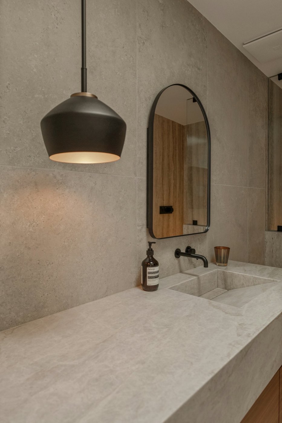 Primary bath in warm limestone with black arched mirror and pendant